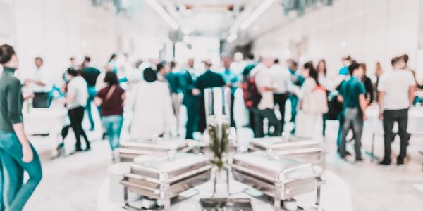 Blurred image of a buffet setup with people mingling in the background.