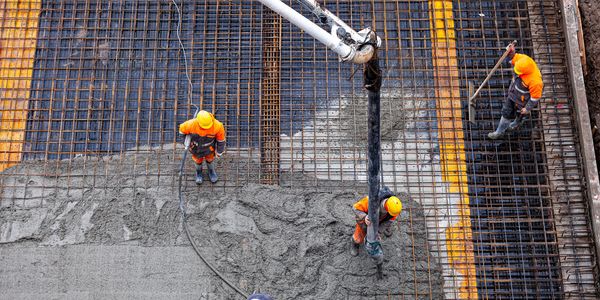 Construction workers pouring and leveling concrete over steel rebar framework.