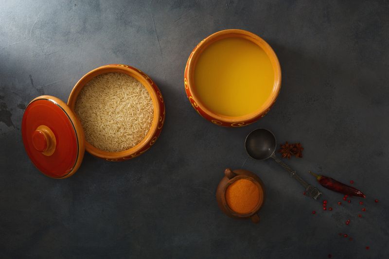 Homemade ghee, rice in a ceramic pot, red peppers and turmeric spices. Top view.