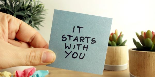 Hand holding a note saying "It starts with you".