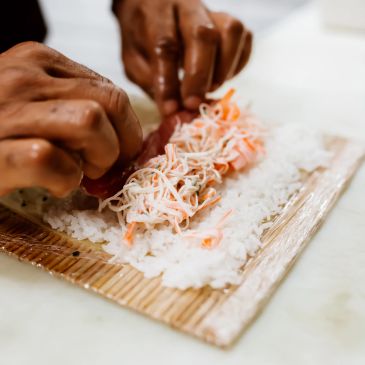 Hands rolling sushi with crab and rice on a bamboo mat.