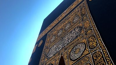 Close-up of the Kaaba's door with intricate gold calligraphy against a clear blue sky. At Reverts Umrah we will talk you through each and every step of your Umrah journey