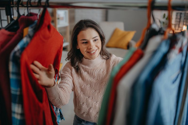 Attractive young woman is choosing clothes in light room. Girl in wardrobe.
