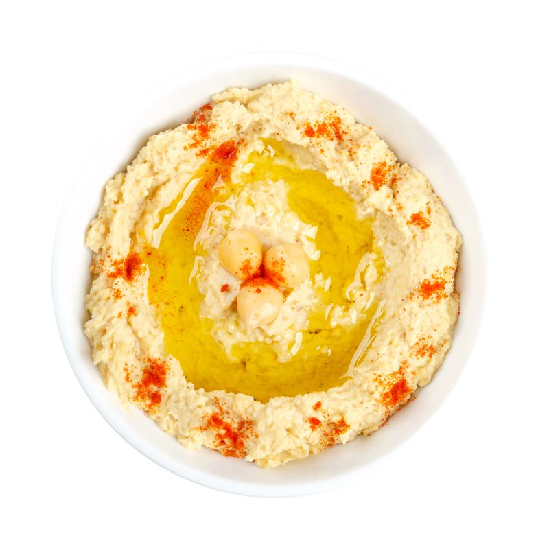 Hummus dip with paprika powder and olive oil, in a white bowl. Middle Eastern dip, spread or savory dish made of cooked, mashed chickpeas, blended with tahini, lemon juice and garlic. Close-up, photo.