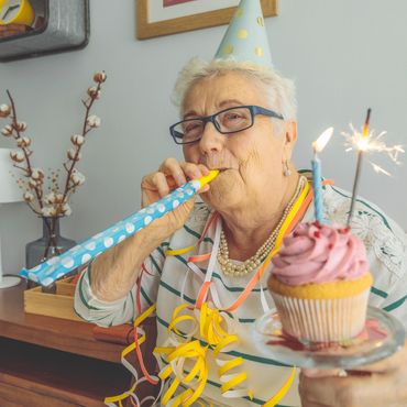 Elderly woman celebrating with a party hat, cupcake, and party blower.