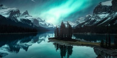 A serene lake with snowy mountains, northern lights, and a large moon in the sky.