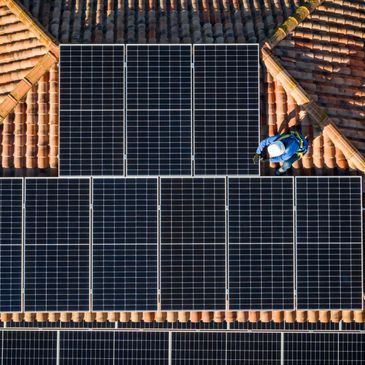 Workers install solar panels on a tiled roof under bright sunlight.