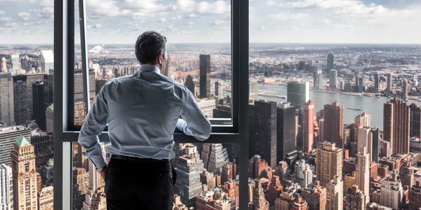 Business professional gazing out a high-rise window at a panoramic city skyline.