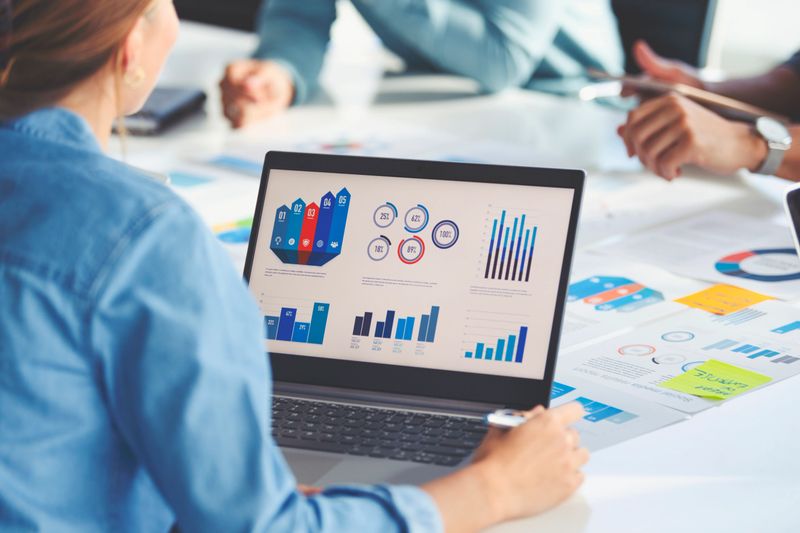 Multi racial group of people working with Paperwork on a board room table at a business presentation or seminar. The documents have financial or marketing figures, graphs and charts on them. There is a laptop with graph and chart data