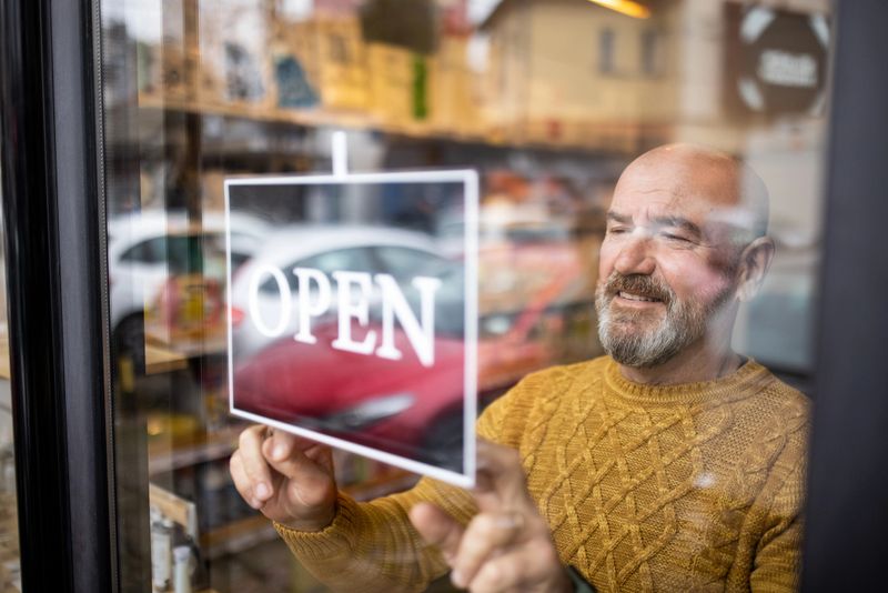 Caucasian male owner of the retail shop for home goods, puts the open sign and open the door of the store