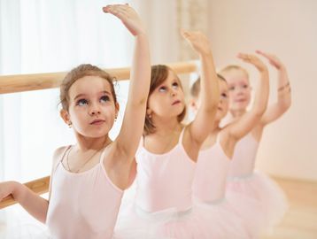 Young girls practicing ballet at a barre, raising their arms gracefully.