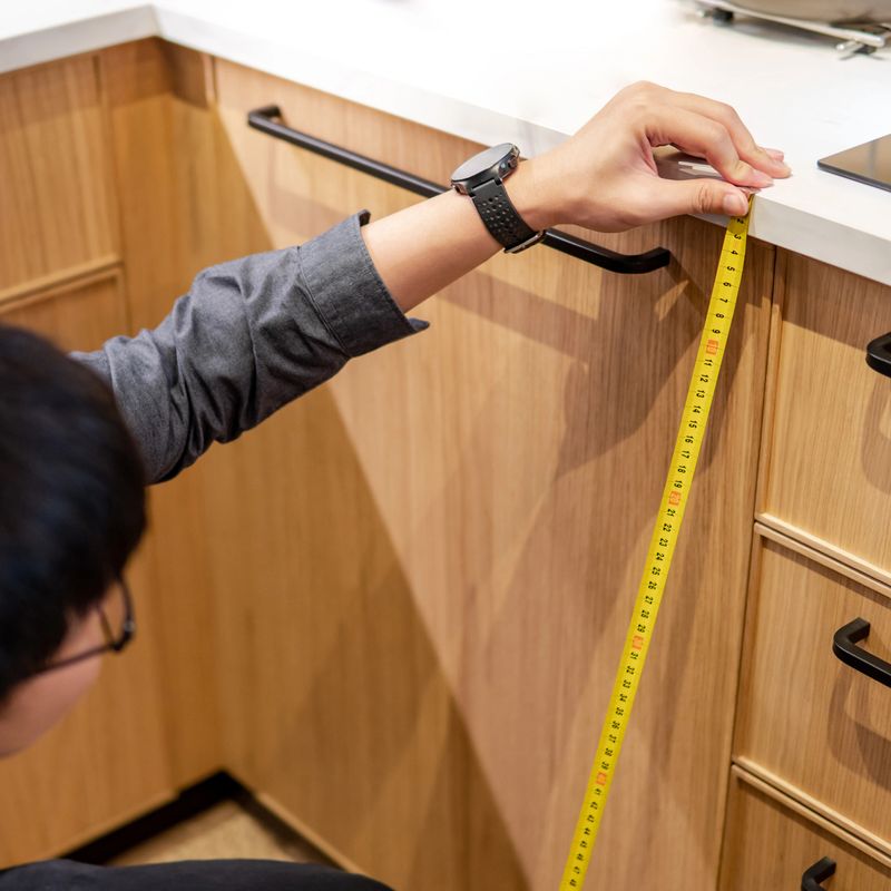 Young Asian man using tape measure for measuring drawer on wooden kitchen counter in showroom. Shopping furniture for home improvement. Interior design concept