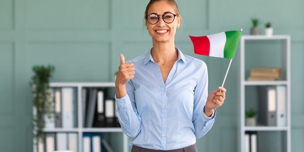 Smiling woman holding Italian flag and giving thumbs up in office.