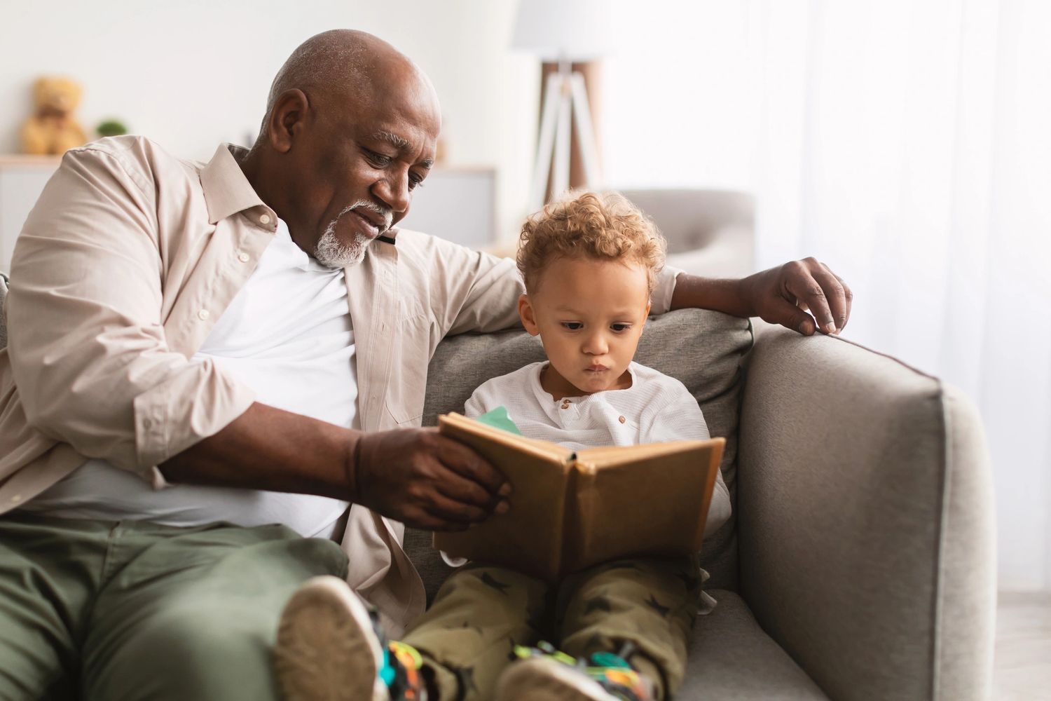 Grandfather reading a book with his grandson on a couch.
