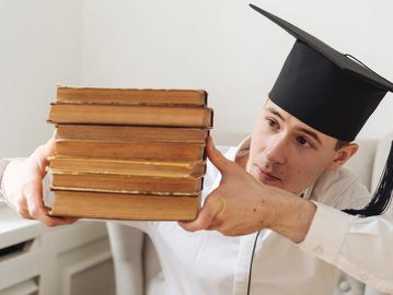 Graduate holding a stack of old books with focus and determination.