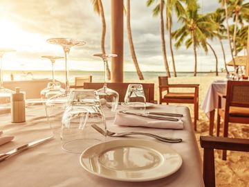 Elegant beachside dining setup with glasses and plates at sunset.