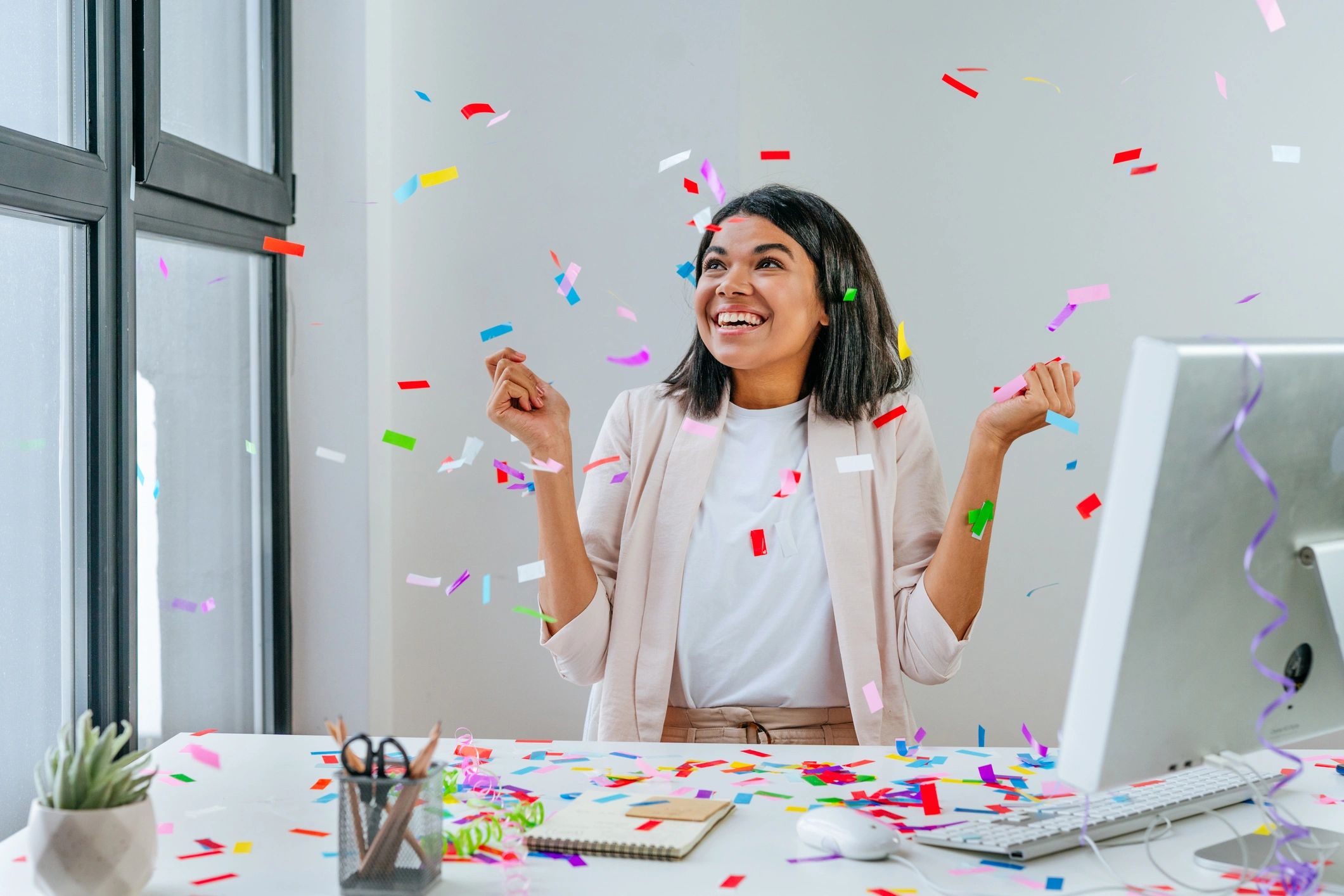 Mujer sonriente celebrando con confeti en una oficina.