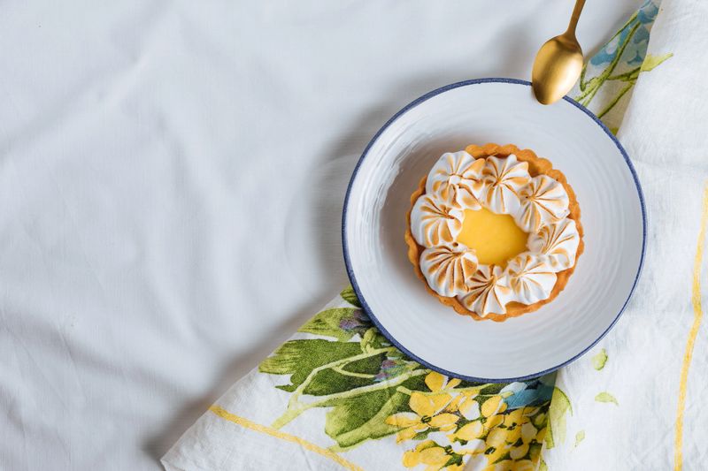 Lemon tart decorated with wiped cream. Decorated with flowers and different cloths and golden spoon. Lemon custard cream and sweet dough. Traditional french dessert.
