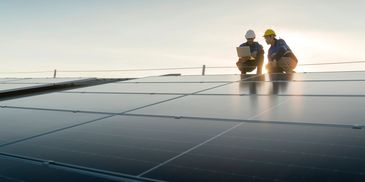 Two workers inspecting solar panels at sunset.