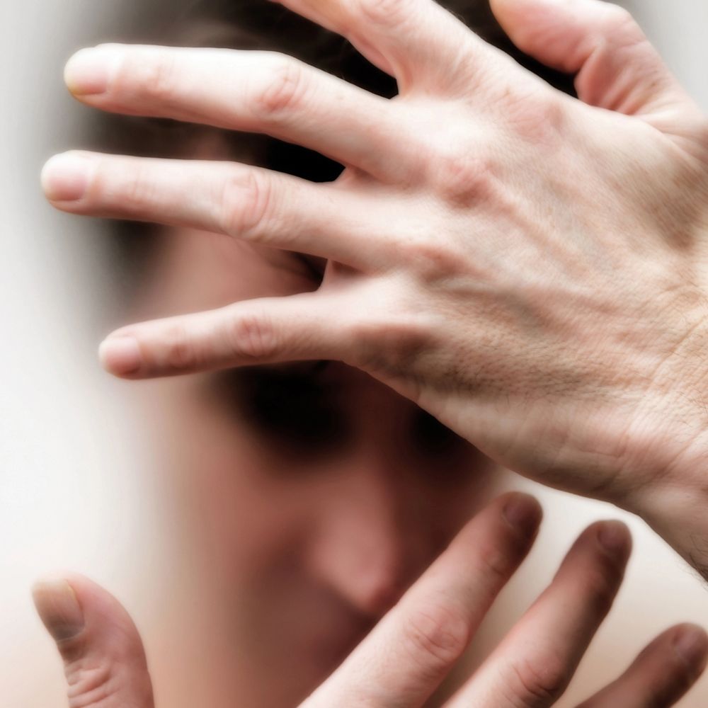 A person shielding their face with hands in a blurred photo.
