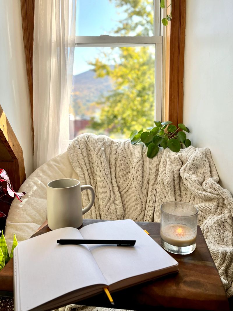 A cozy reading nook with a chair next to a window and a journal to write on. Conveys the ideas of self care and wellness.