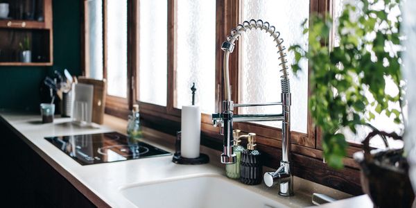 Modern kitchen sink with a flexible chrome faucet and natural light from wooden windows.