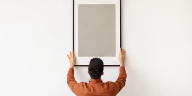 Man hanging a blank picture frame on a white wall.