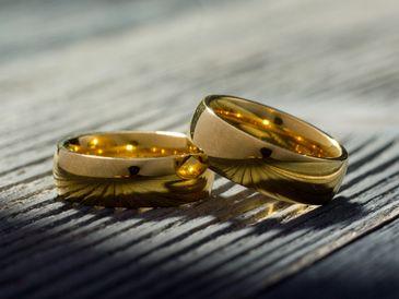 Two gold wedding rings on a wooden surface with soft lighting.