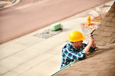 Construction worker inspecting a roof while wearing a yellow helmet.