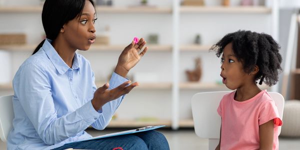 A woman teaching a girl with colorful letters, both making expressive faces.