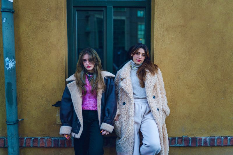 Portrait of young stylish young women leaning against wall on street