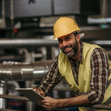 Smiling industrial worker in safety gear holding a tablet.