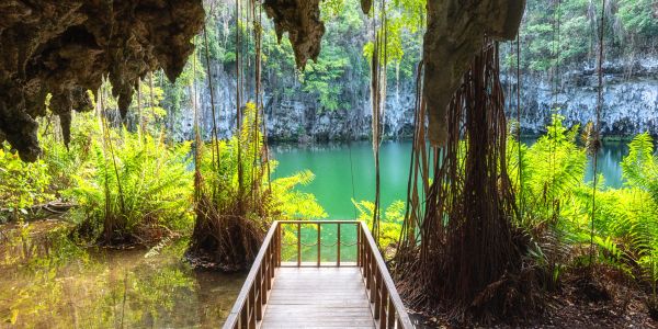 Wooden pathway inside a cave overlooking a turquoise water pool.
