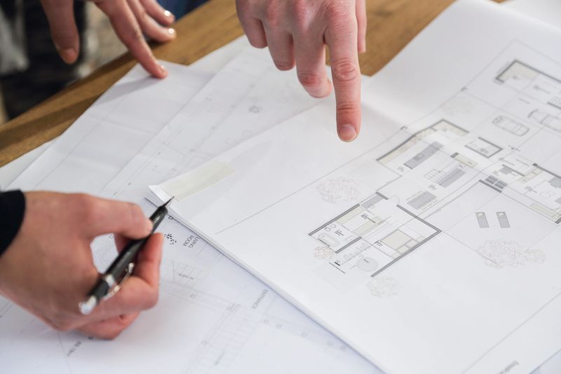 Businessman and businesswoman hands showing, looking and making notes on blueprints and talking about plans.
