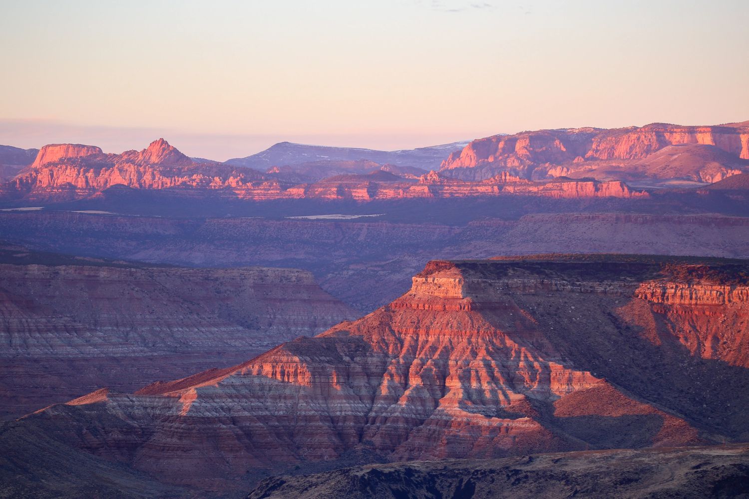 Sunset illuminates layered rock formations in a vast desert canyon.