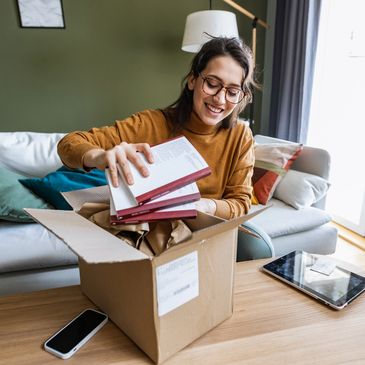 Woman happily unpacking books from a box in a cozy living room.