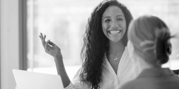 Two women engaged in a happy conversation at an office.