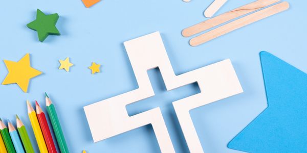 Paper cross surrounded by colored pencils and star shapes on blue background.