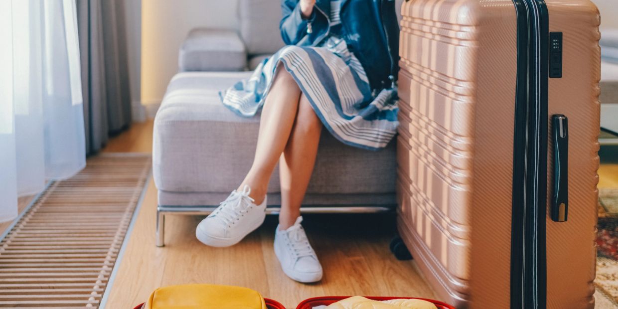 Person sitting on a couch with a large suitcase and open packed luggage.
