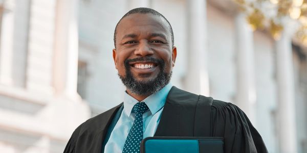 Smiling graduate holds diploma outside a classical building.