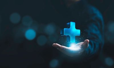 Hand holding glowing blue medical cross symbol.
