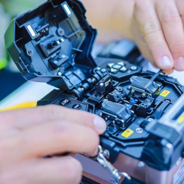 Hands working on a fiber optic fusion splicer.