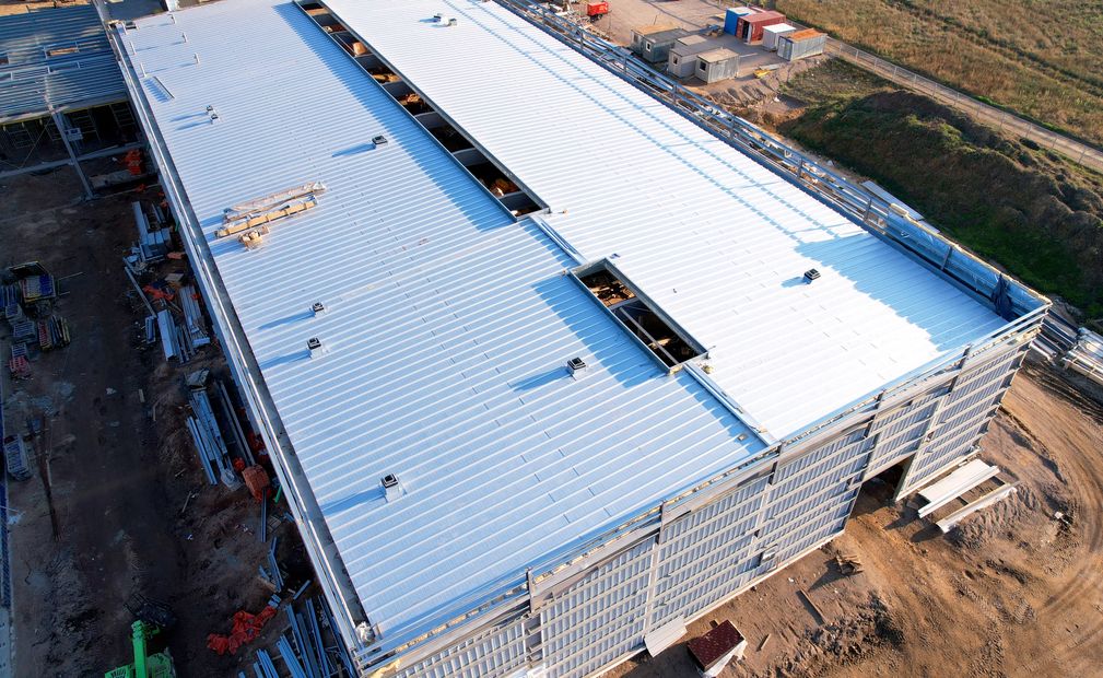 Aerial view of a large building with a corrugated metal roof and brick wall.