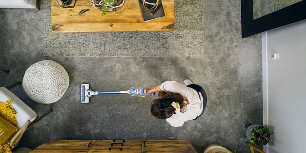 Overhead view of a woman vacuuming a cozy living room with a cordless vacuum.