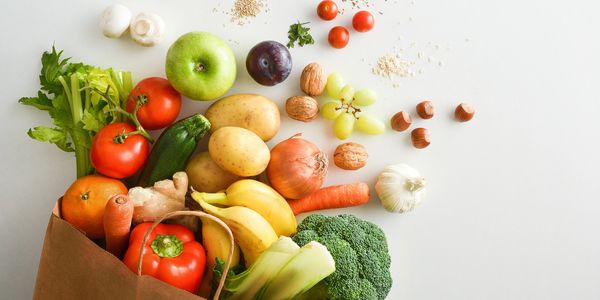 Brown bag overflowing with fresh fruits, vegetables, nuts, and herbs.
