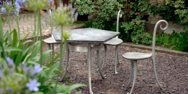 Mesa y sillas de metal en un jardín con plantas.