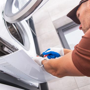 Technician repairing a front-load washing machine with tools and gloves.