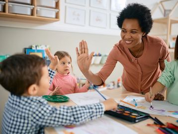 Teacher giving a high-five to a child during a classroom art activity.