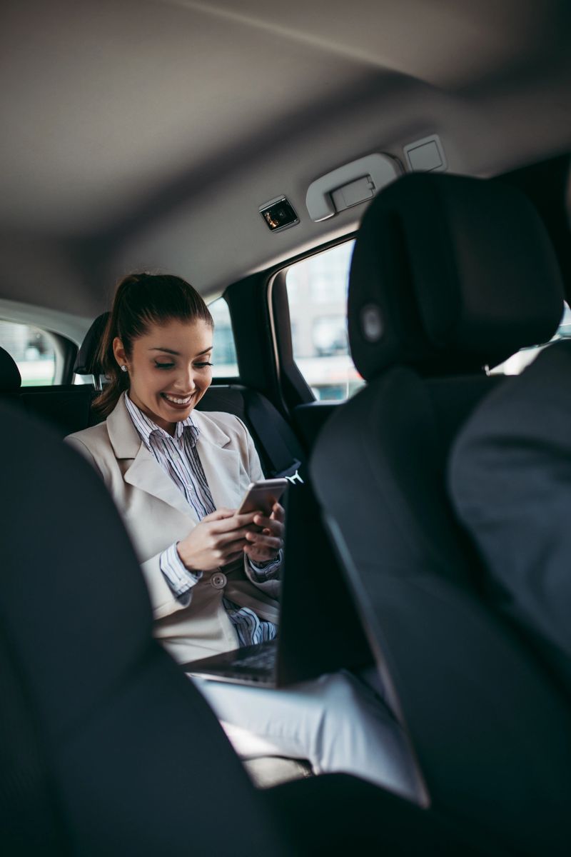 Good looking senior driver and young businesswoman sitting on backseat in luxury car. They are talking and smiling. Transportation in corporate business concept.