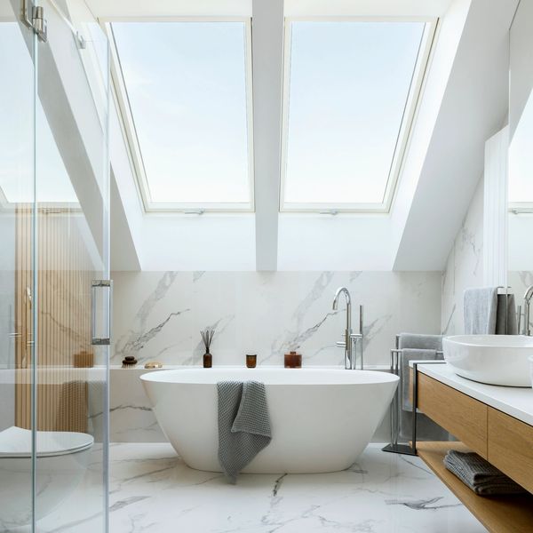 Modern bathroom with a freestanding tub under skylights and marble flooring.